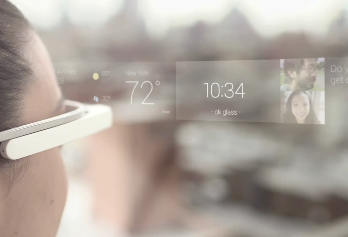 person is wearing a pair of smart - glasses. On the transparent display of the glasses, various information is shown. The time displayed is 10:34, and the temperature is 72 degrees. There are also location - related indicators such as "Amsterdam 23" and "New York 57", along with weather icons suggesting rain in Amsterdam and partly - cloudy in New York. Additionally, there is a small image of two people on the right side of the display, and the text "ok glass" is visible at the bottom, indicating a voice - command activation feature. The background is blurred, focusing on the information presented on the smart - glasses.