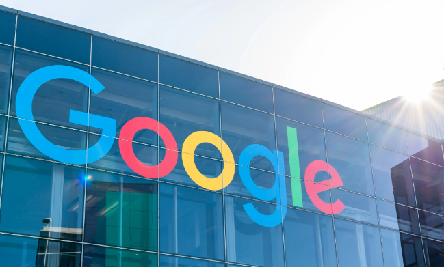 The Google logo displayed prominently on the glass facade of a modern office building, with sunlight streaming from the upper right corner, symbolising innovation and technological leadership.