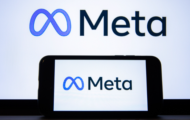The image shows the Meta logo, featuring a stylised blue infinity symbol followed by the word 'Meta' in bold black letters. The logo is displayed on both a smartphone screen and a larger background, highlighting the brand's modern and digital identity.