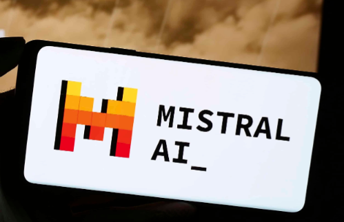The image shows a smartphone screen displaying the Mistral AI logo, featuring a stylised letter 'M' in shades of orange, yellow, and red, alongside the text 'MISTRAL AI_' on a white background.